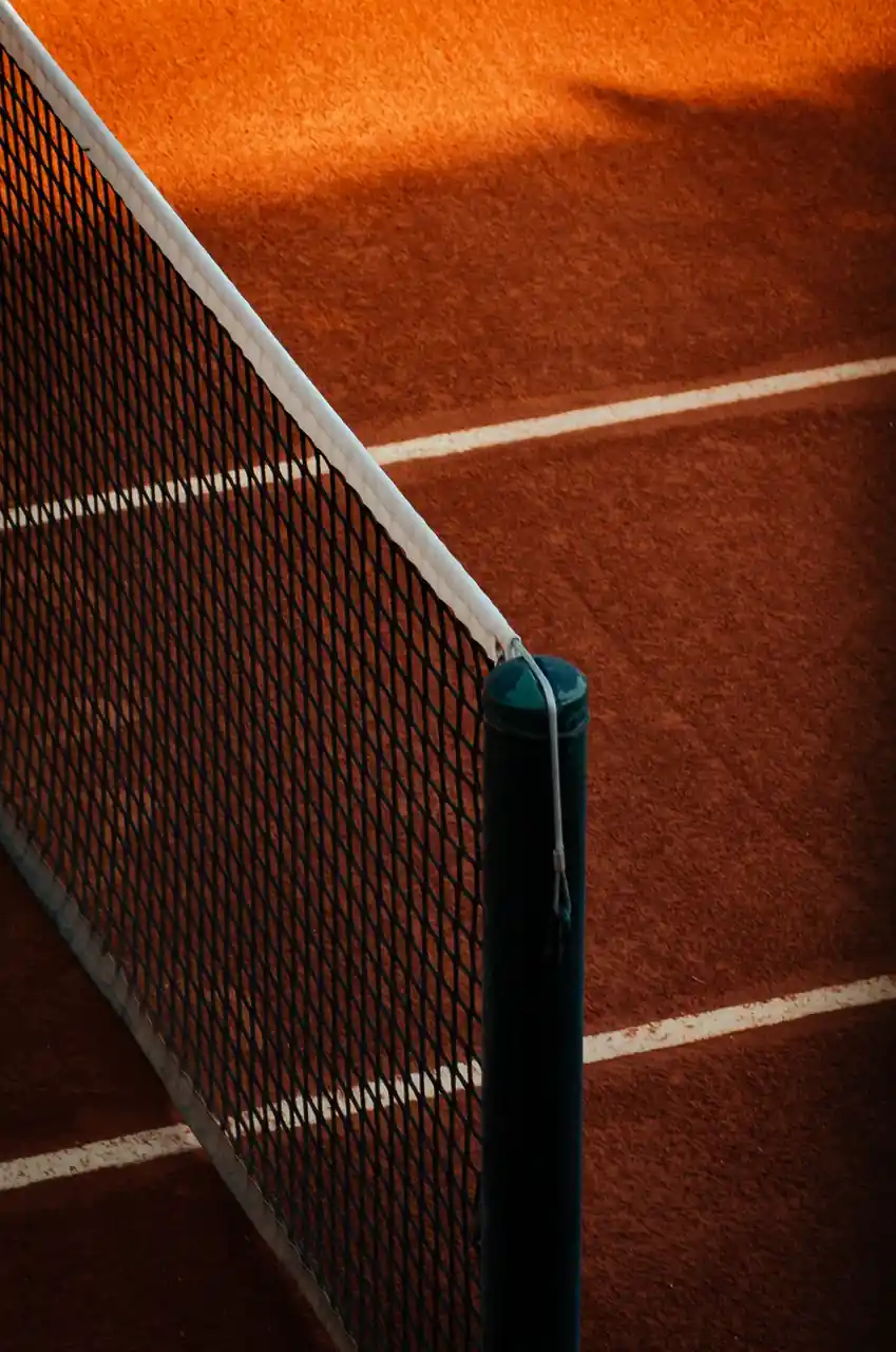 Clay tennis court with net and shadows under soft light