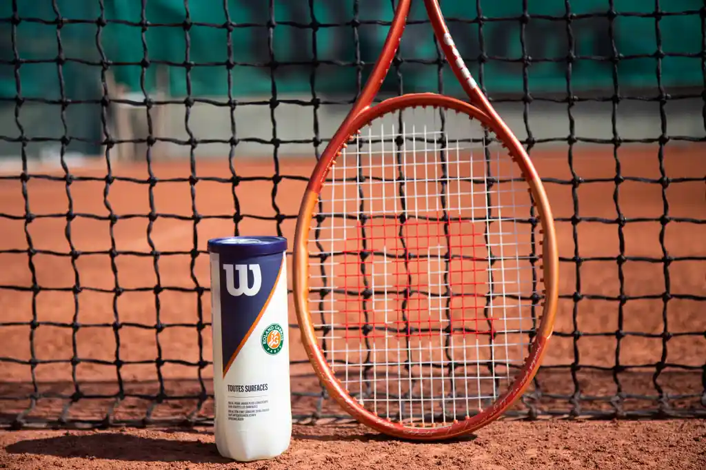 Tennis racket and ball can in front of a net on a clay court