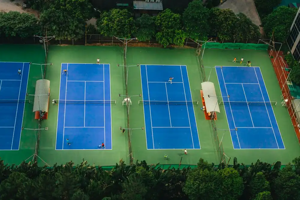High angle perspective of players engaging in an afternoon tennis match surrounded by greenery
