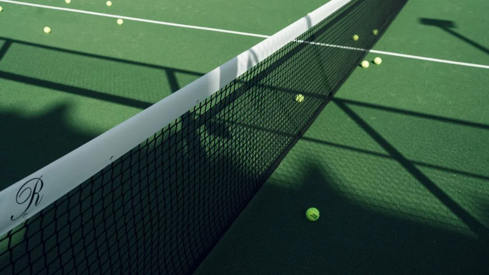 Outdoor tennis court net casting clean shadows along pristine green playing surface