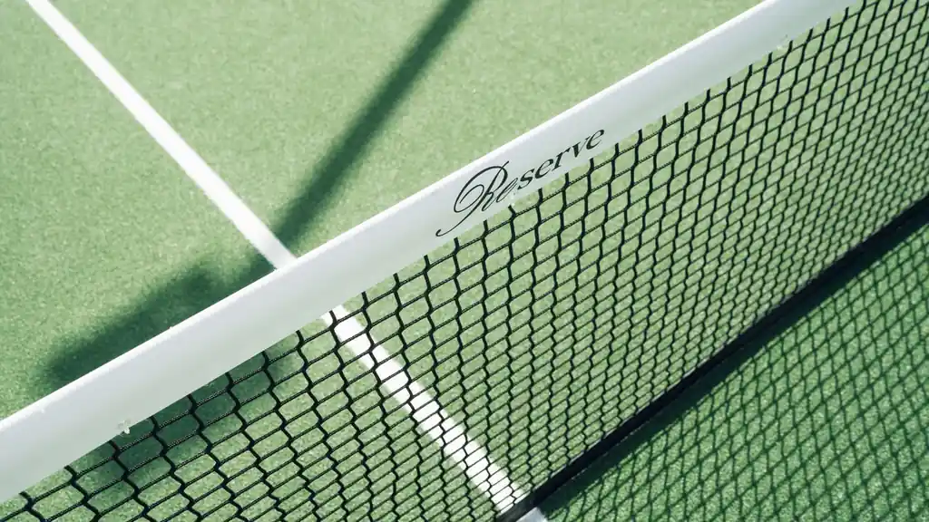 Close-up of a tennis net on a green court casting soft afternoon shadows