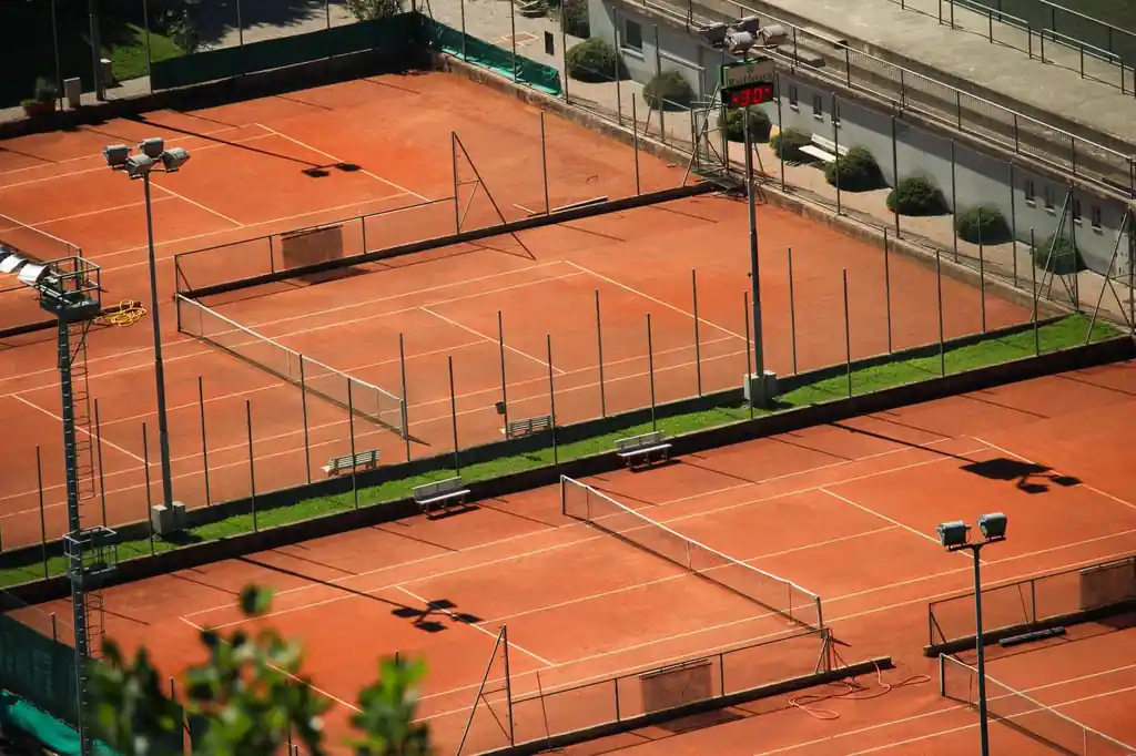 Aerial shot of red clay tennis courts on a sunny day with geometric shadows