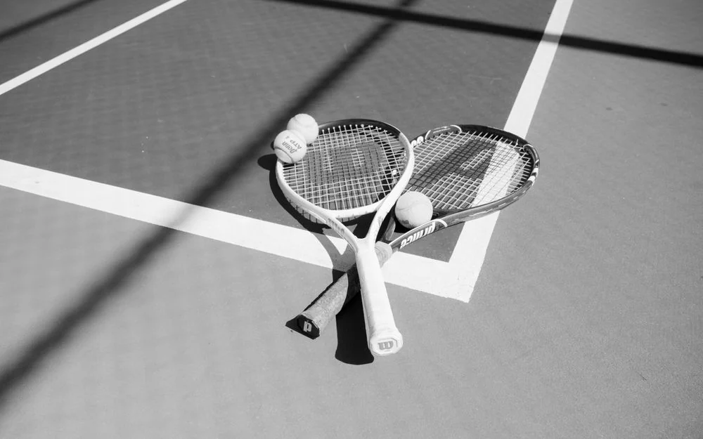Classic tennis rackets and tennis balls arranged neatly on a sunlit court