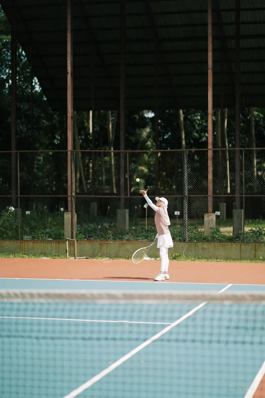 Tennis player in traditional white attire prepares to serve on outdoor court
