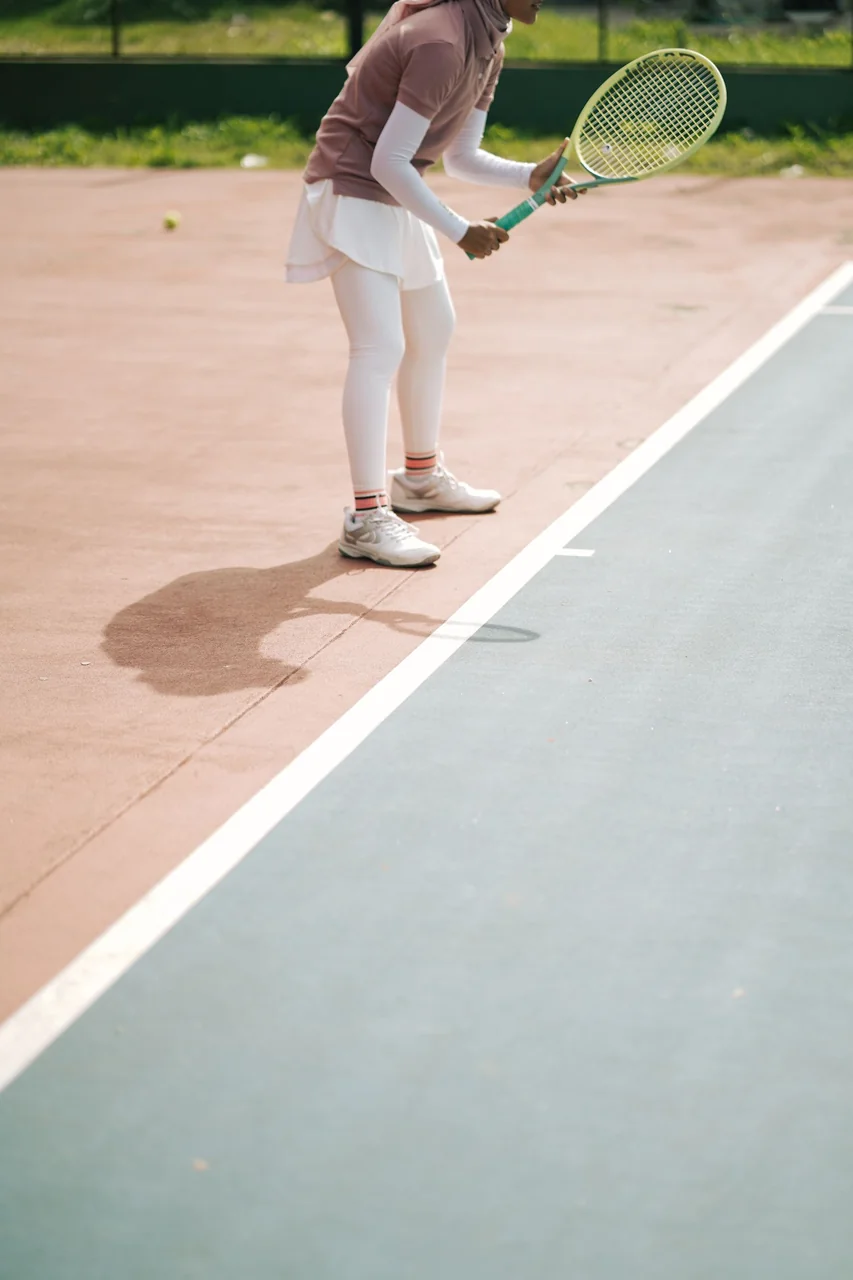 Female tennis player prepares to serve on an outdoor court, dressed in proper sportswear