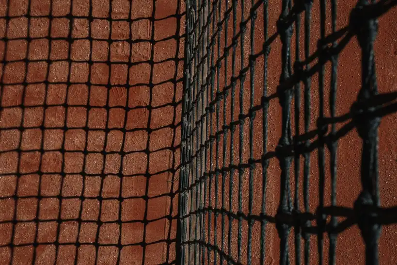Detailed close-up of a tennis net casting shadows on a clay court surface during the day