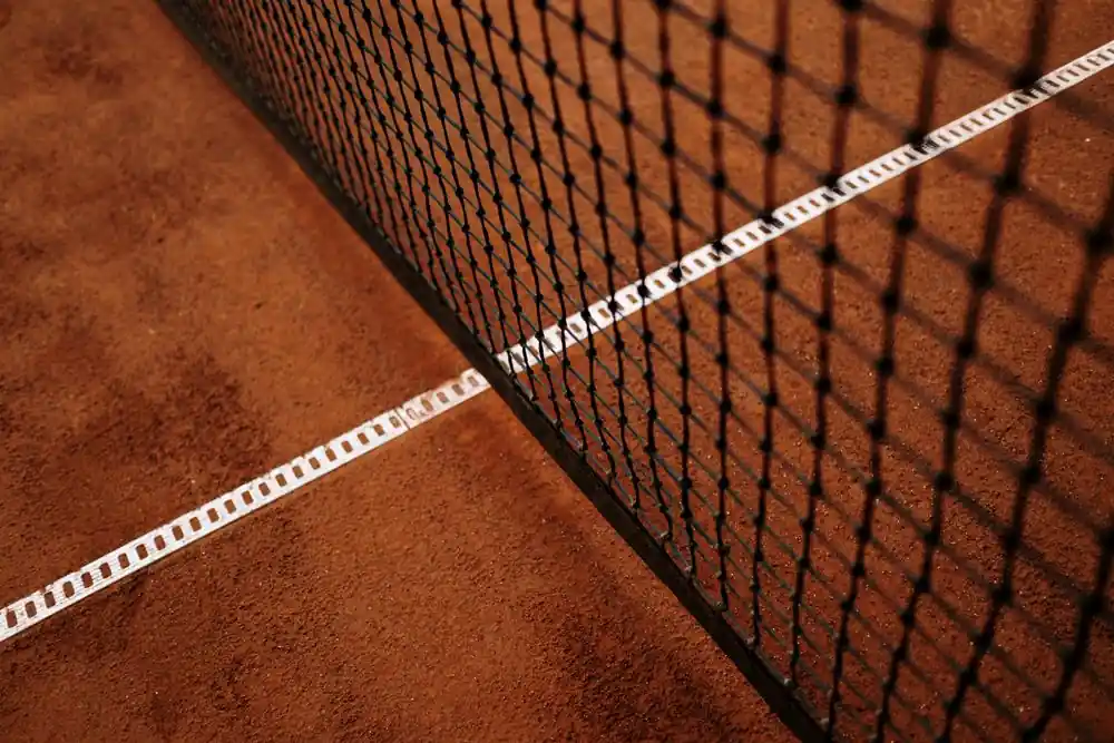 Detailed close-up of a clay tennis court featuring the net and white baseline