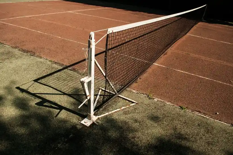 Detailed close-up of a classic tennis net against sun-dappled court grounds